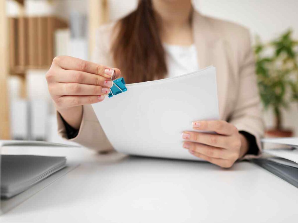 Pessoa organizando documentos com clipe de papel, representando o conceito de comprar um projeto de mestrado