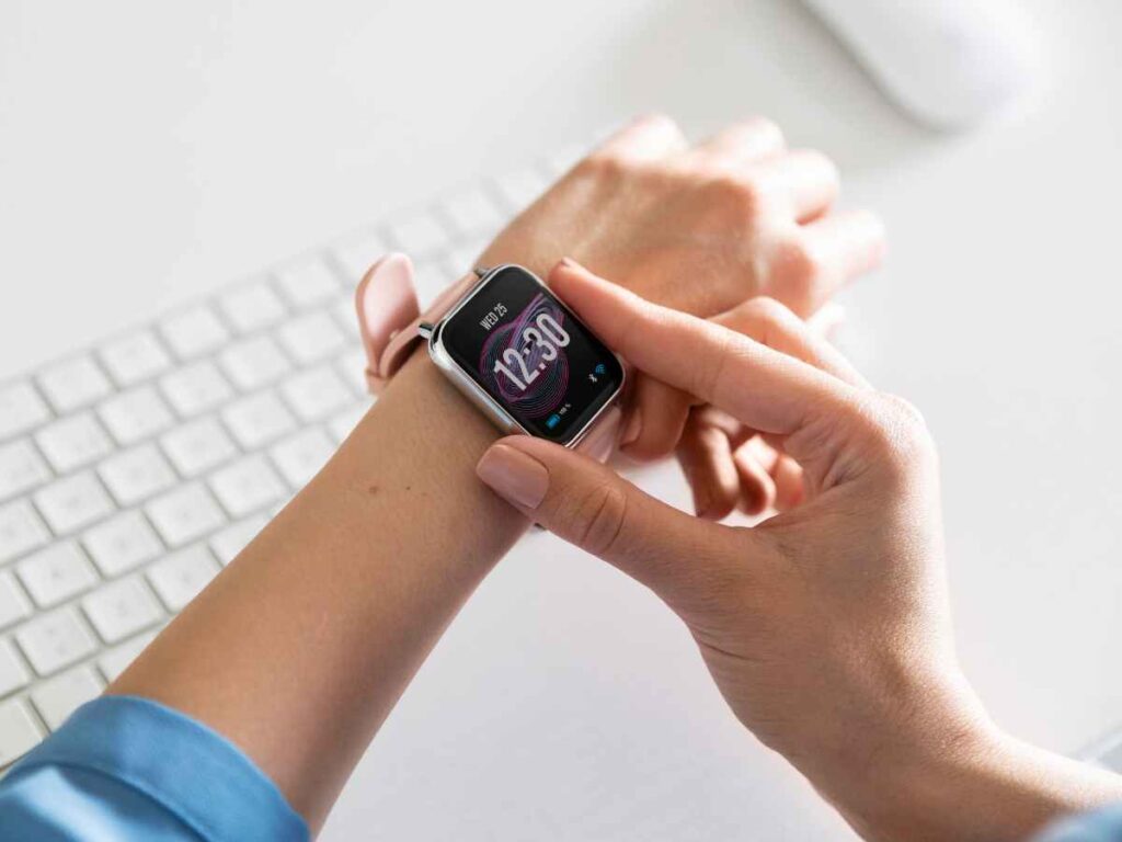 Pessoa verificando o horário em um smartwatch enquanto trabalha no computador.