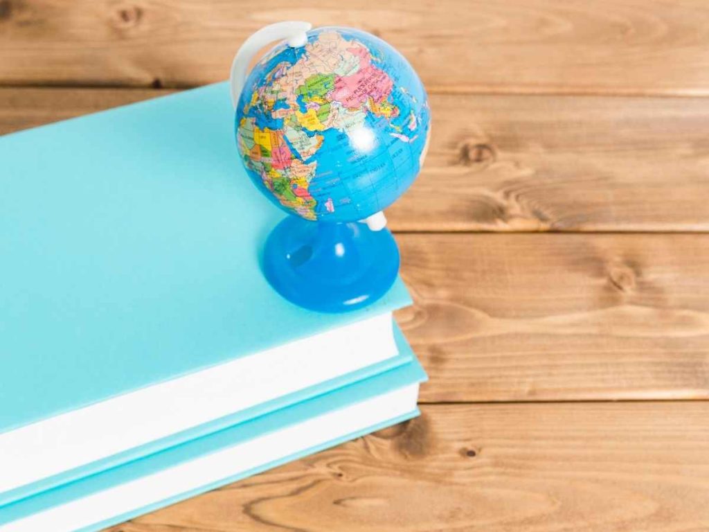 Globo terrestre sobre pilha de livros azuis sobre mesa de madeira