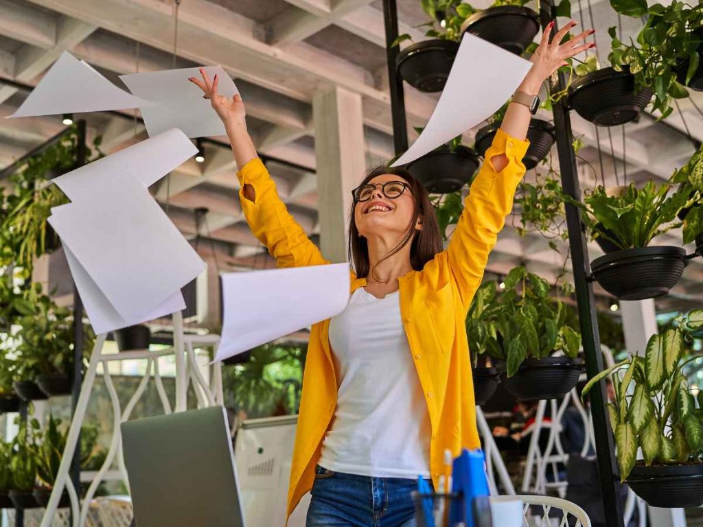 Mulher jogando papéis ao ar com sorriso e energia positiva.